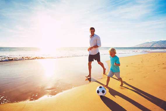 father and son playing soccer on the beach